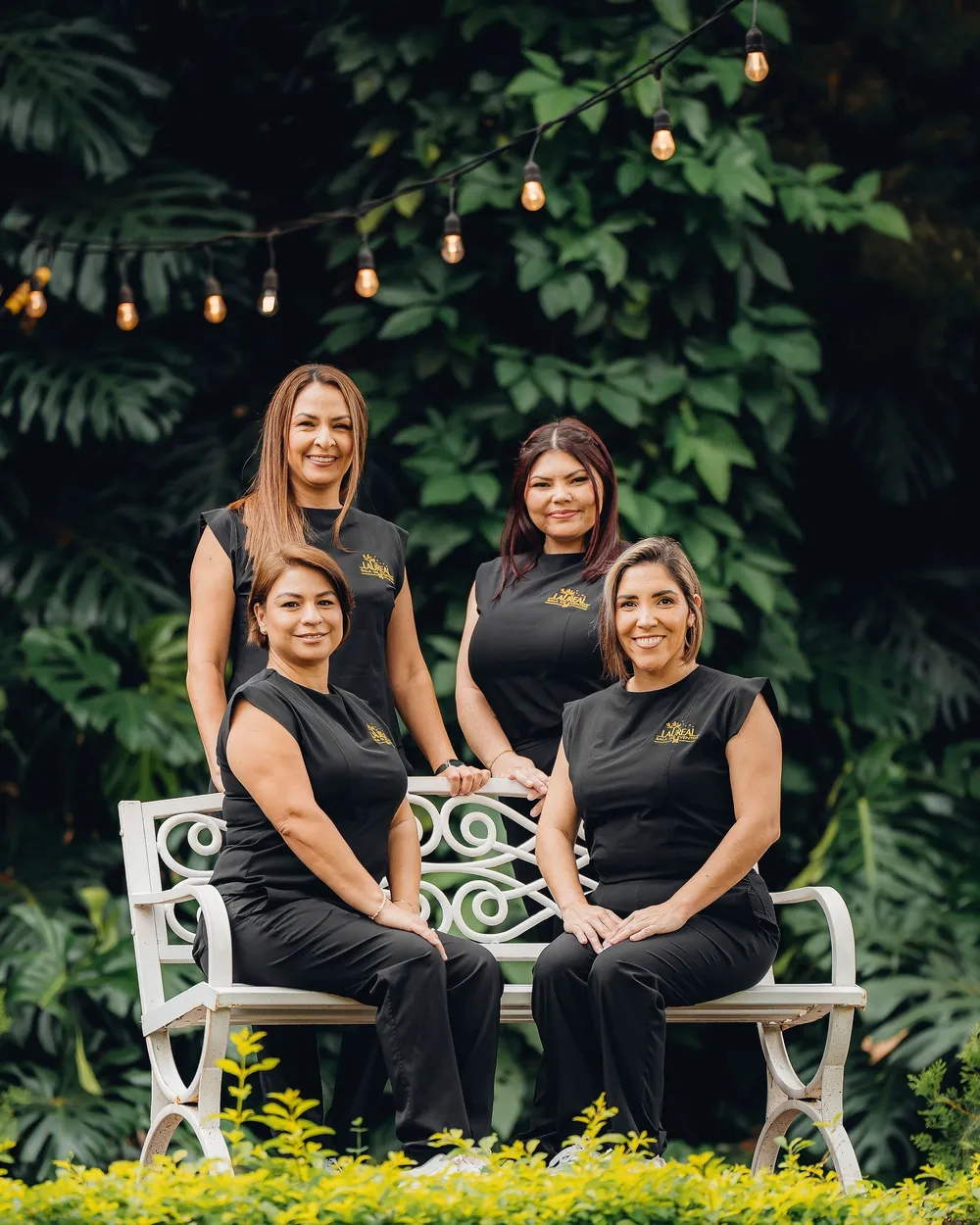 El equipo de Sala de Eventos Laureal: cuatro integrantes con el uniforme de la casa, sentadas en una banca del jardín bajo luces colgantes
