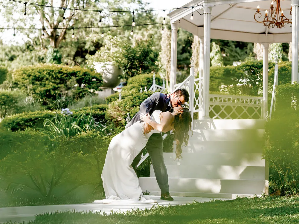 Novios besándose sobre el prado con el Gazebo Jardín al fondo