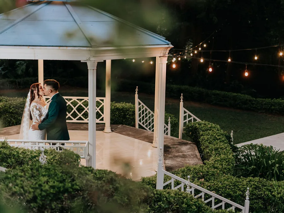 El Gazebo Jardín iluminado de noche con luces colgantes y los novios dentro