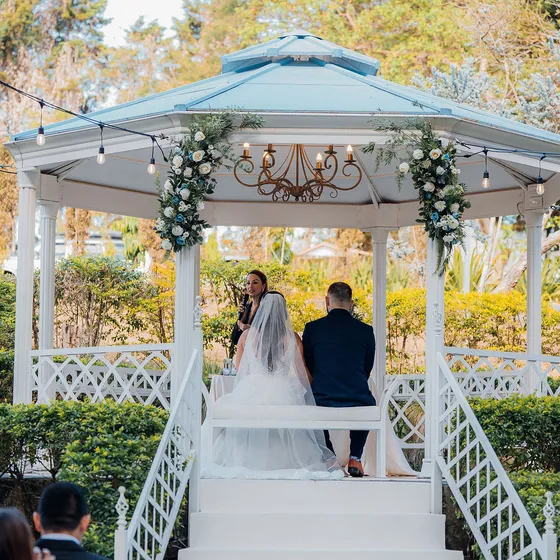Novios en la escalinata del Gazebo Jardín, decorado con arco floral, durante la ceremonia