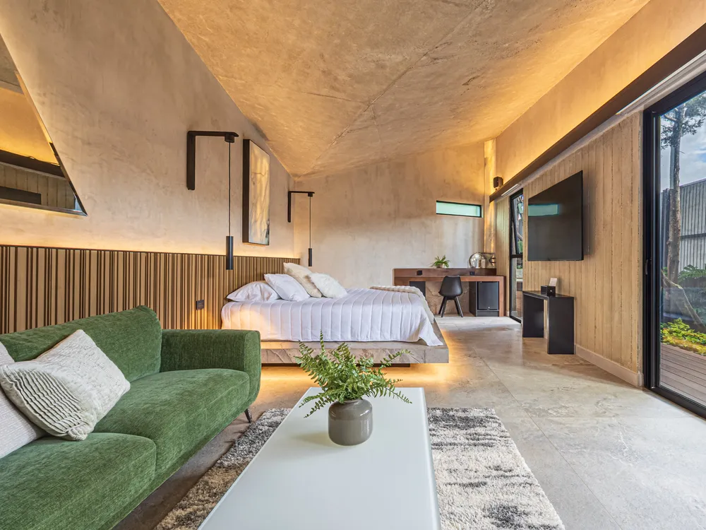 Habitación de Nebulae con sofá, cama y luz cálida bajo el techo inclinado de concreto
