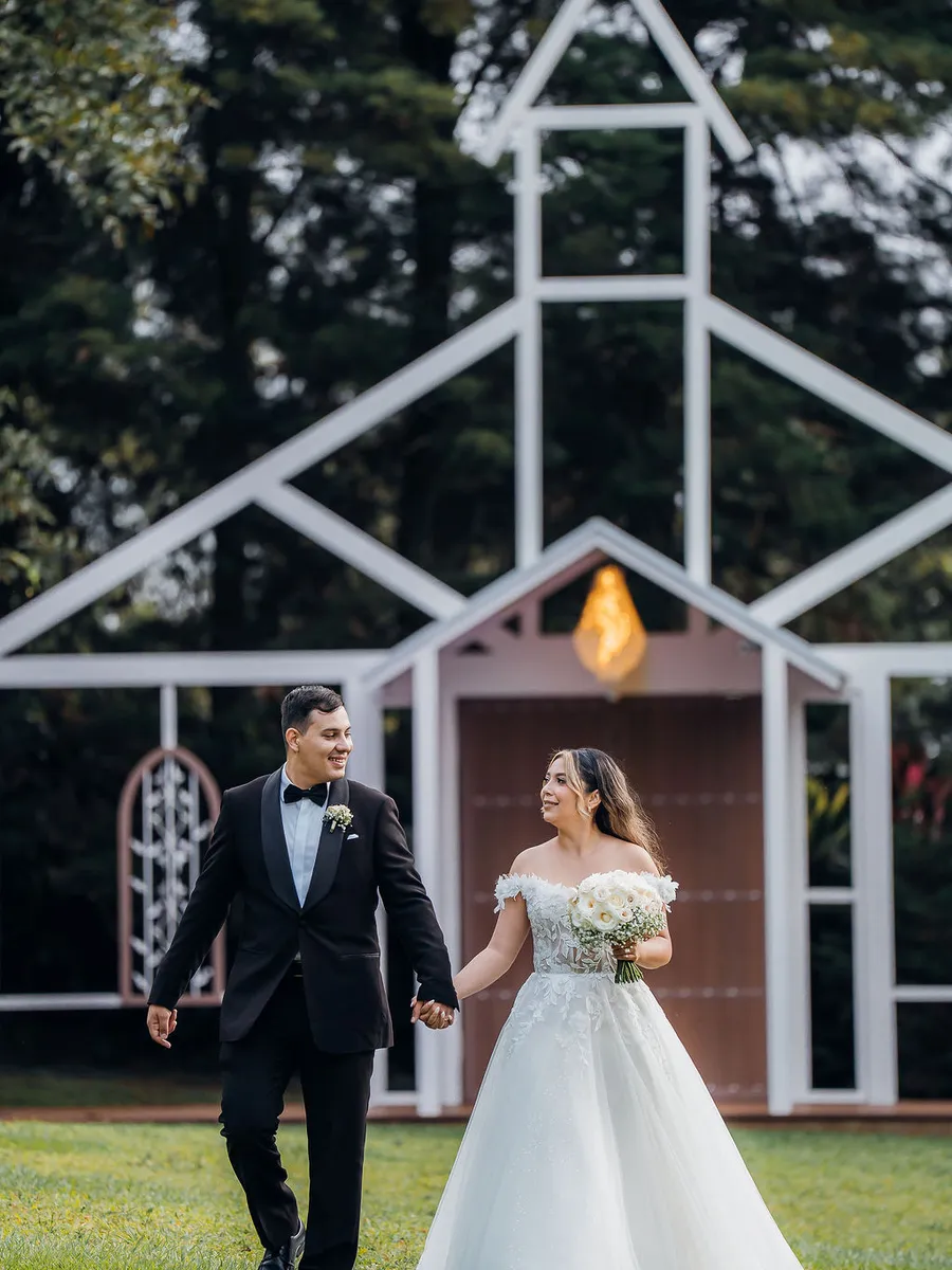 Novios caminando sobre el prado con la Fachada de la Iglesia iluminada detrás