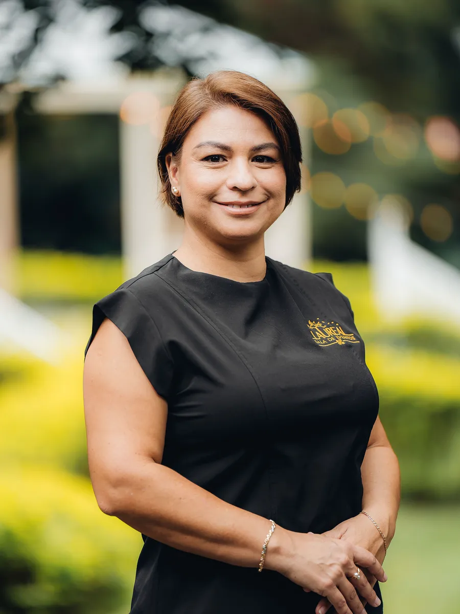 Laura Bogantes, la persona detrás de Sala de Eventos Laureal, con uniforme negro y el logotipo dorado de Laureal, en los jardines de la finca