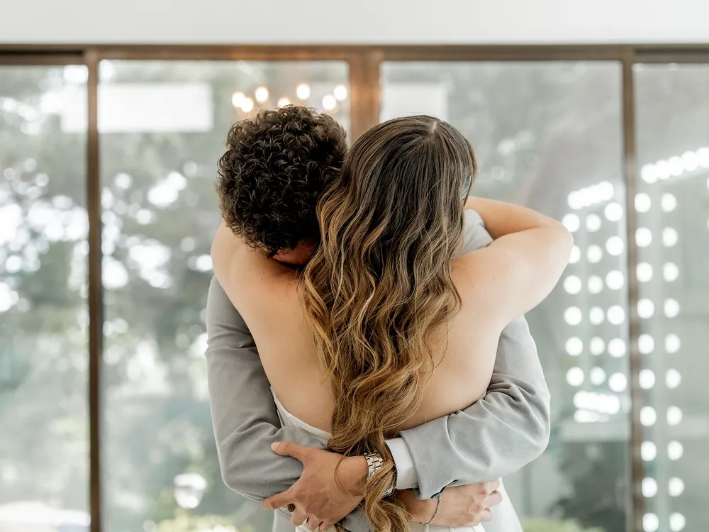 Abrazo de la novia con un familiar frente al ventanal del Salón de Maquillaje