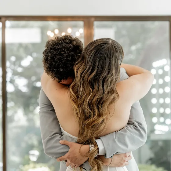 Abrazo de la novia con un familiar frente al ventanal del Salón de Maquillaje