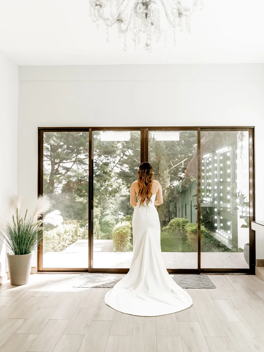 Novia de espaldas frente al ventanal del Salón de Maquillaje, con el jardín al fondo