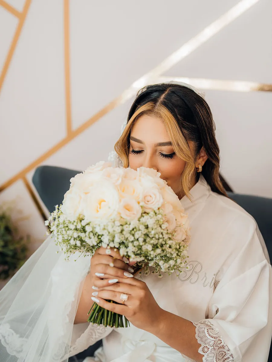 Novia con su ramo de rosas blancas en bata, antes de vestirse