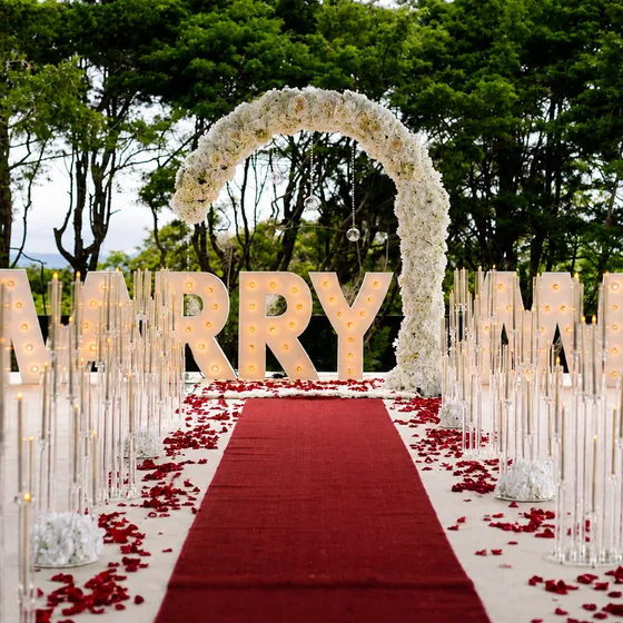 Montaje de propuesta de matrimonio con letras iluminadas, arco floral y alfombra roja