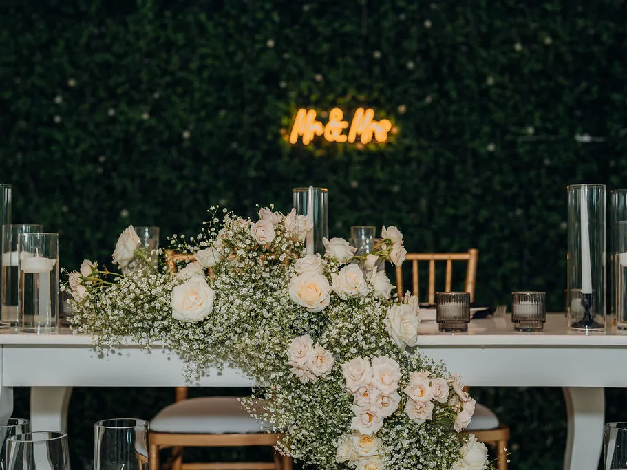 Mesa principal con arreglo floral y rótulo de neón sobre el muro verde
