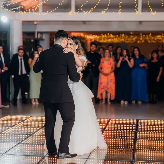Primer baile de los novios sobre la pista dorada, rodeados de invitados